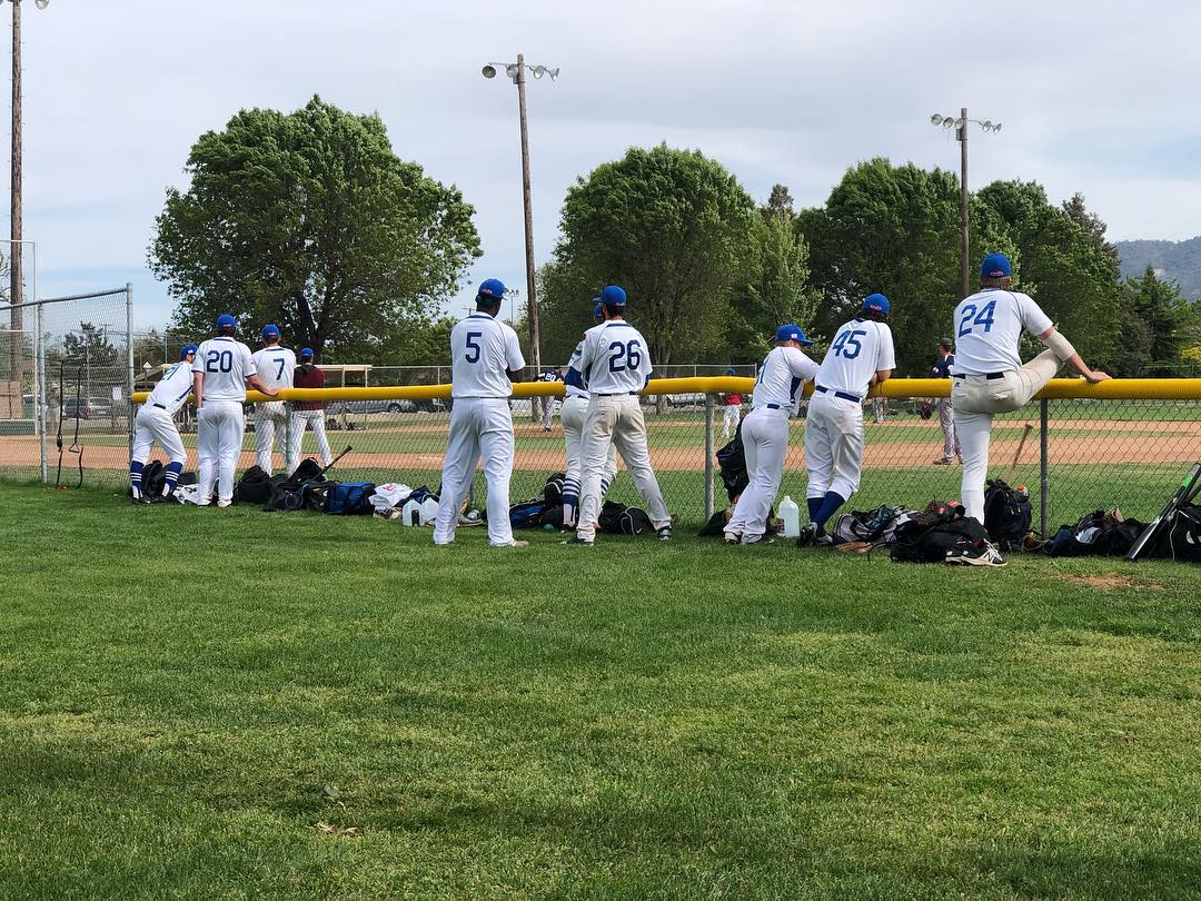 Bakersfield Train Robbers baseball players standing against fence watching the game